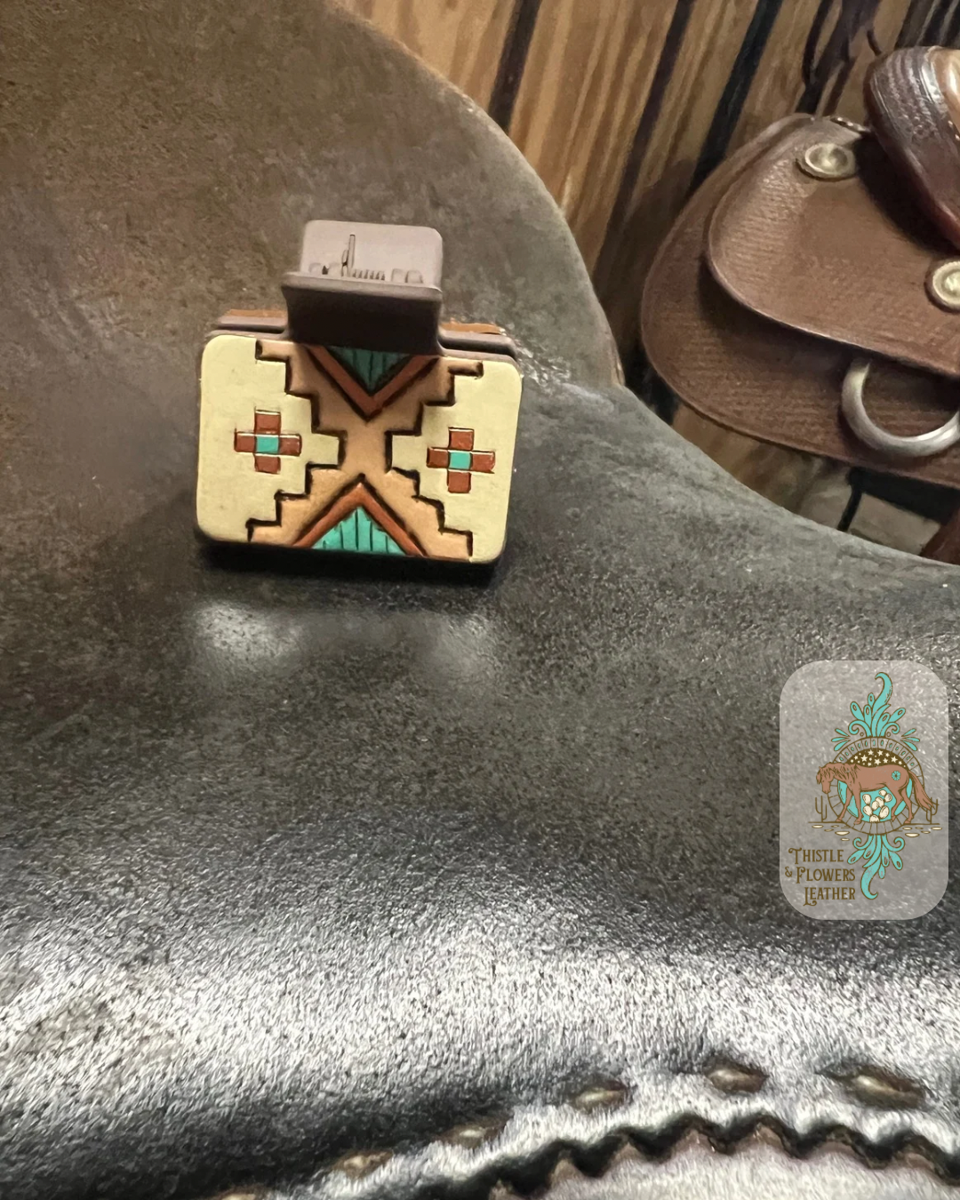 Medium brown base hairclip with hand tooled and painted leather patch. Patch is tooled with a southwestern design and the paint colors are cream, turquoise, and metallic copper. Hairclip is resting on saddle seat. Logo is in the bottom right of photo.