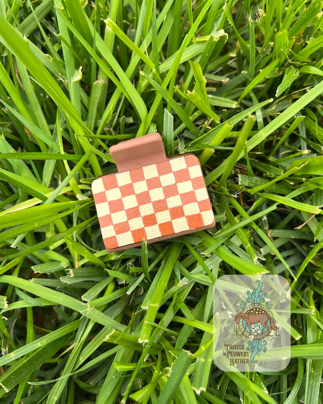 Brown base Hairclip with hand painted brown and cream checkerboard pattern leather patches. Photographed on grass with logo on bottom right of photo.