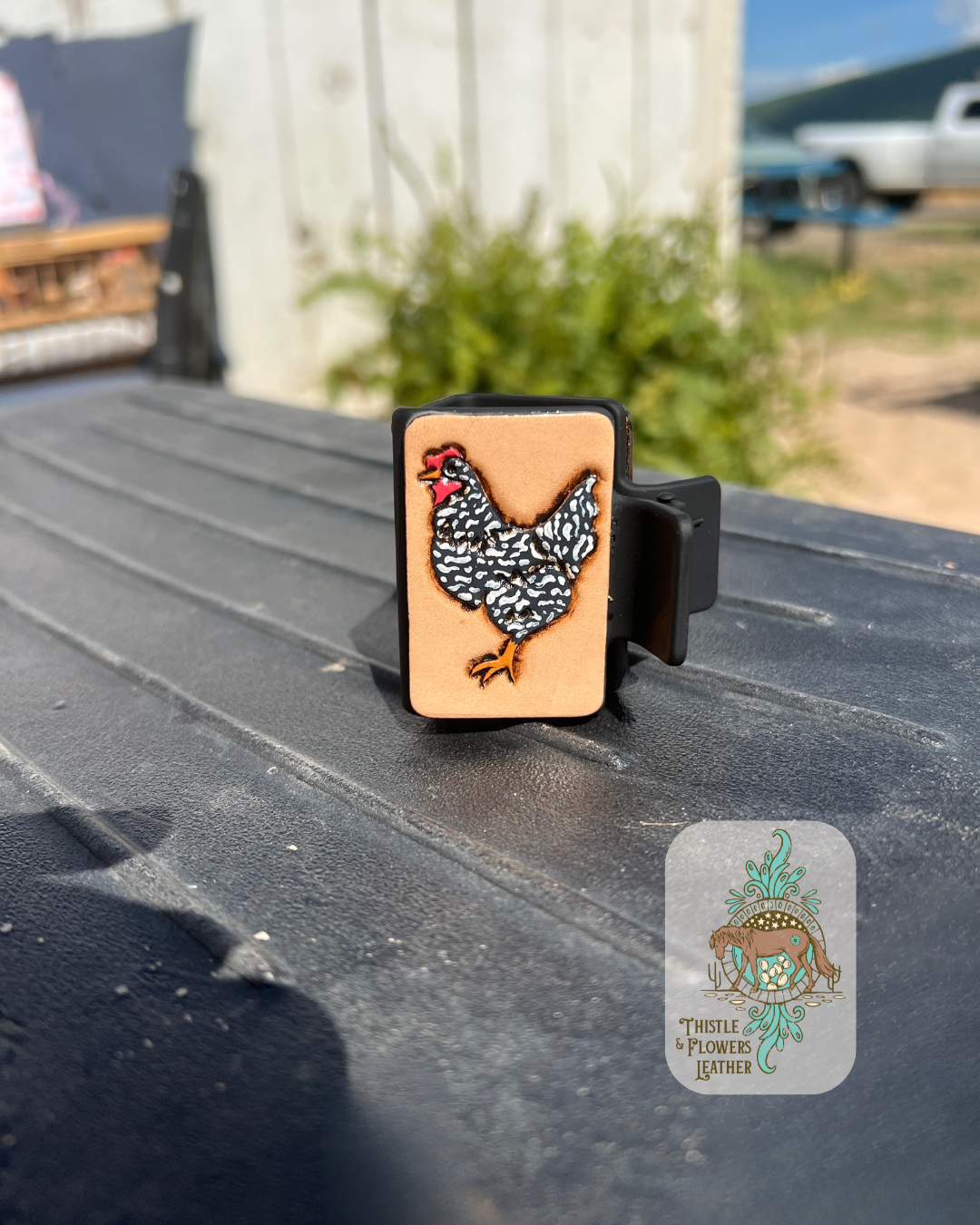 Medium sized black base hairclip with a hand tooled and painted chicken on it. Chicken is painted black, white, yellow, and red. Hairclip is sitting on a mounting block in arena. Logo is in bottom right of photo.