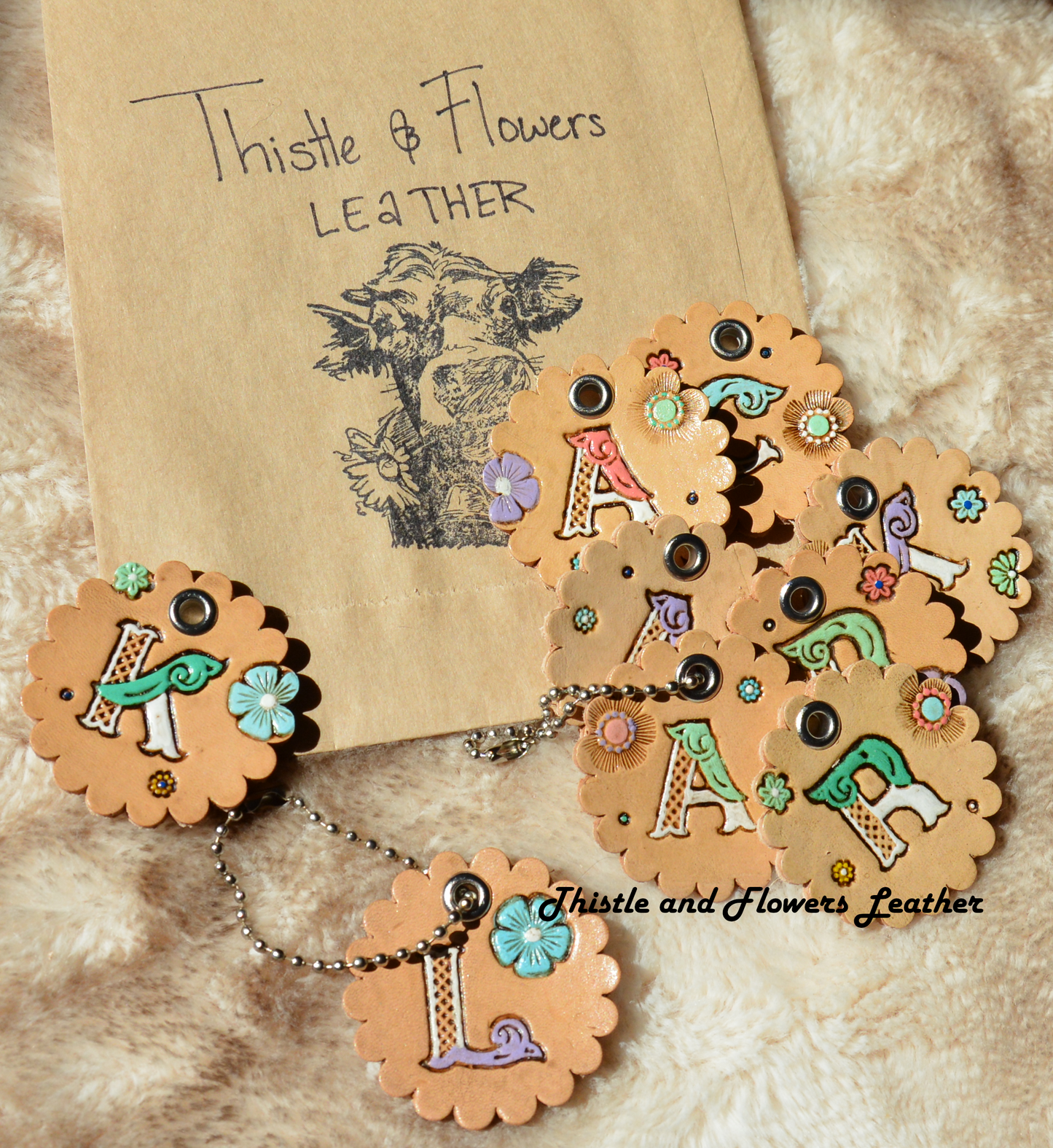 Tooled leather keychain with beaded connector. Scalloped edges, letters, "K" "L" "R" "A" "C" "R" "K" "A" "A" with white and other colors. Multicolored flowers.. Antiqued. Each letter is on a seperate keychain with different flowers.