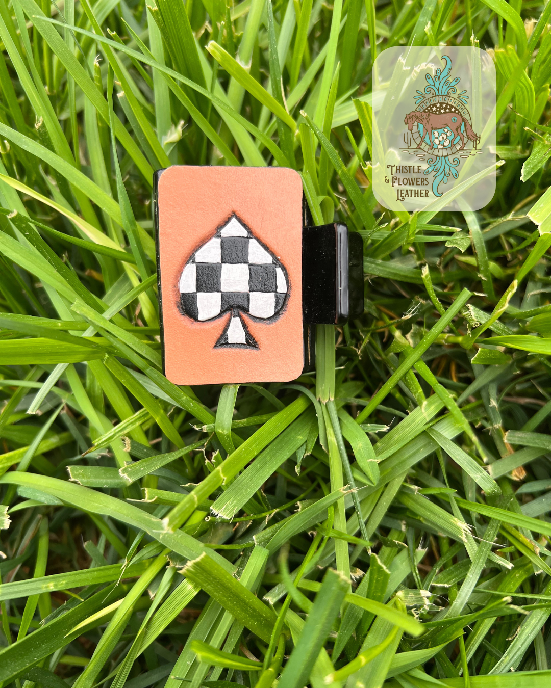 Black base Hairclip with tooled and painted spade design. Spade is painted in a back and white checkerboard pattern. Photographed on grass with logo in top right of photo.