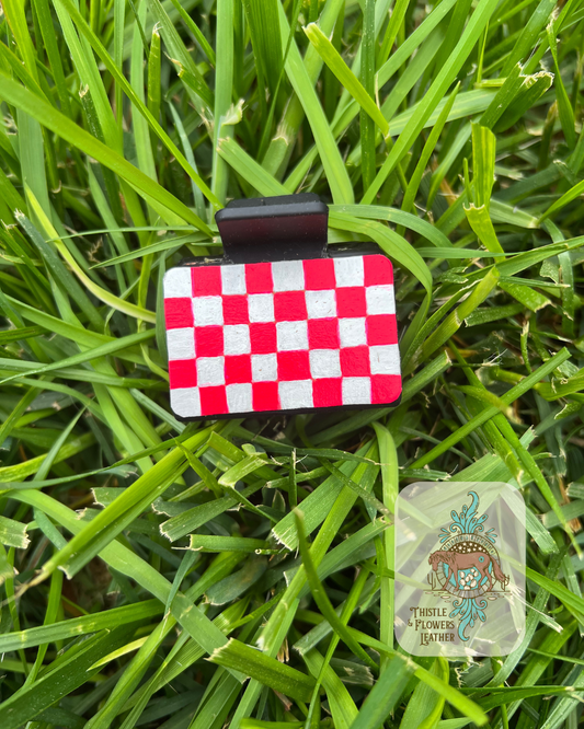 Hand painted hot pink and white checkerboard leather patches on a black hair clip. Photographed on grass with logo in bottom right of photo.