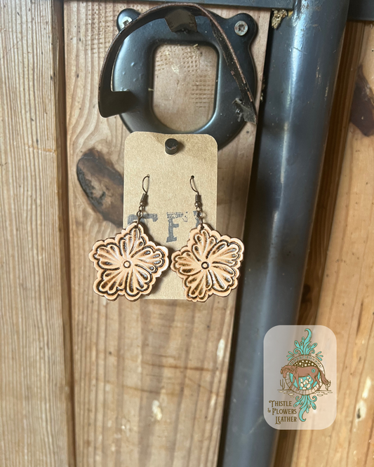 Traditional western tooling flowers cut out as earrings. Earrings are hanging on stall front. Logo is on bottom right of photo. 