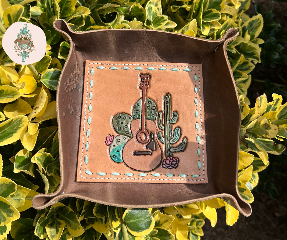 Leather valet tray with a chocolate colored leather exterior and a vegtan center that is tooled and painted. THe tooled image is of an acoustic guitar with cacti around it. The veg-tan also has mint suede buckstich around the border. 