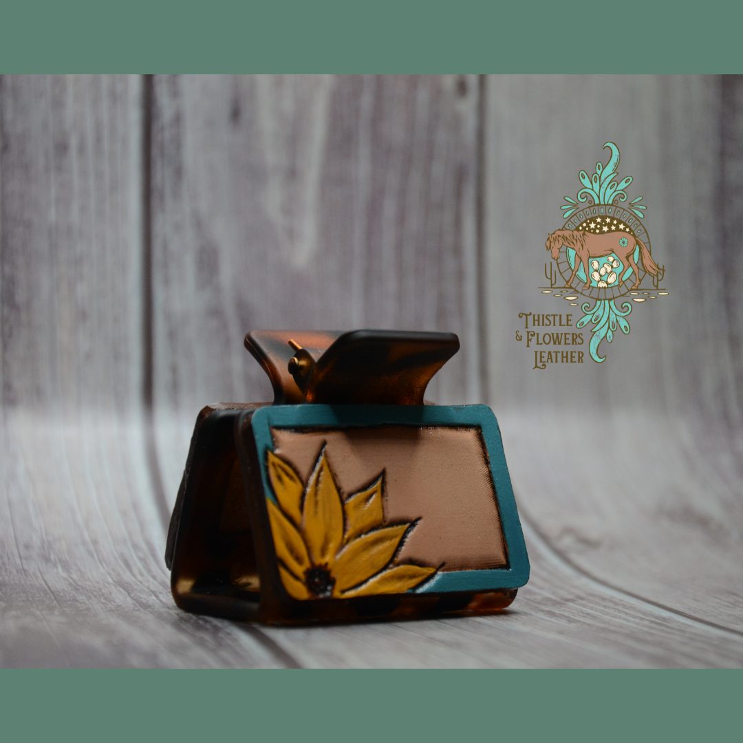 Medium sized tortoiseshell hair clip with a tooled and painted leather patch. Bright golden yellow sunflower 1/2 way showing in the corner, with a bluish turquoise border.