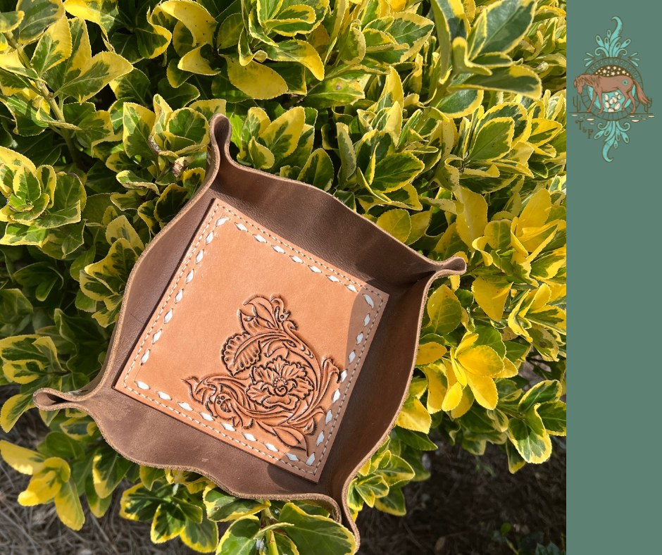 Leather valet tray with chocolate colored brown leather around exterior, and tooled veg tanned center. Tooling is of a western Style flower and scrollwork. The border of the veg tanned center has white buckstitch.