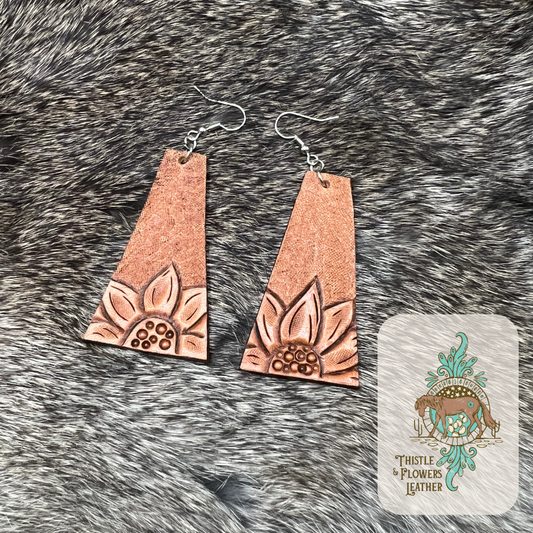 Tooled leather earrings in a trapezoid shape. Top half of leather is tooled to hold a little bit of antique, while the bottom has a tooled sunflower. . Nickel free silver earrings hoops and jump rings. Earrings are on rabbit fur.