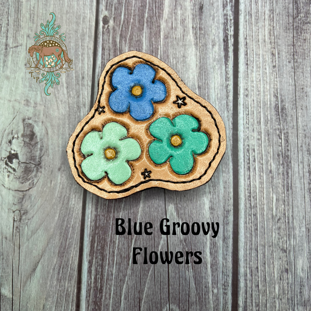 Tooled leather all weather bag charm with 3 tooled flowers on it - one mint, one blue, and one teal. Small white stars are also tooled around the flowers.