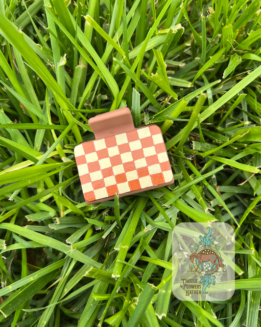 Brown base Hairclip with hand painted brown and cream checkerboard pattern leather patches. Photographed on grass with logo on bottom right of photo.
