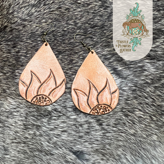 Tooled leather earrings in a teardrop shape. 1/2 of a sunflower is on the bottom half of the earrings.  Nickel free brass colored earrings hoops and jump rings. Earrings are on rabbit fur.