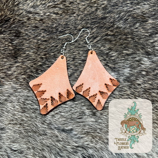 Tooled leather earrings in a diamond shape. Diamond edges are slightly concave. Aztec design is tooled on bottom 2 edges. Nickel free silver earrings hoops and jump rings. Earrings are on rabbit fur.