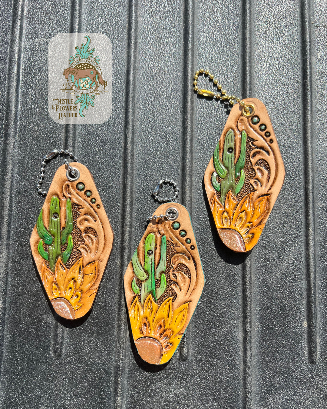 3 sunflower and cactus tooled hotel keychains on a mounting block. Left 2 have silver colored hardware and right one has gold colored hardware. Logo is in top left of photo.