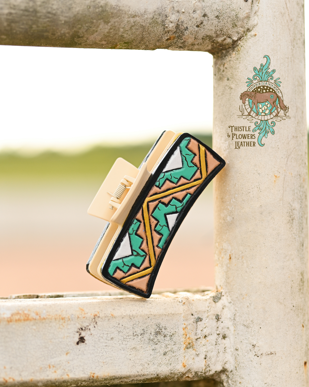 Cream colored large claw clip with tooled and painted leather patches. Design on patches is an Aztec inspired shapes painted like real turquoise with an opal triangle in the center, and a metallic gold line zig-zagging around the shapes.