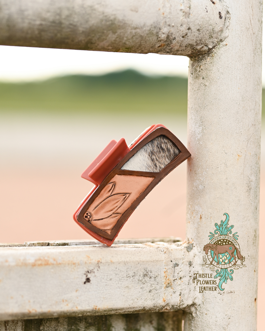 Rust colored hair clip with a tooled leather patch. Leather patch has a cowhide inlay, with white and salt & pepper cowhide.