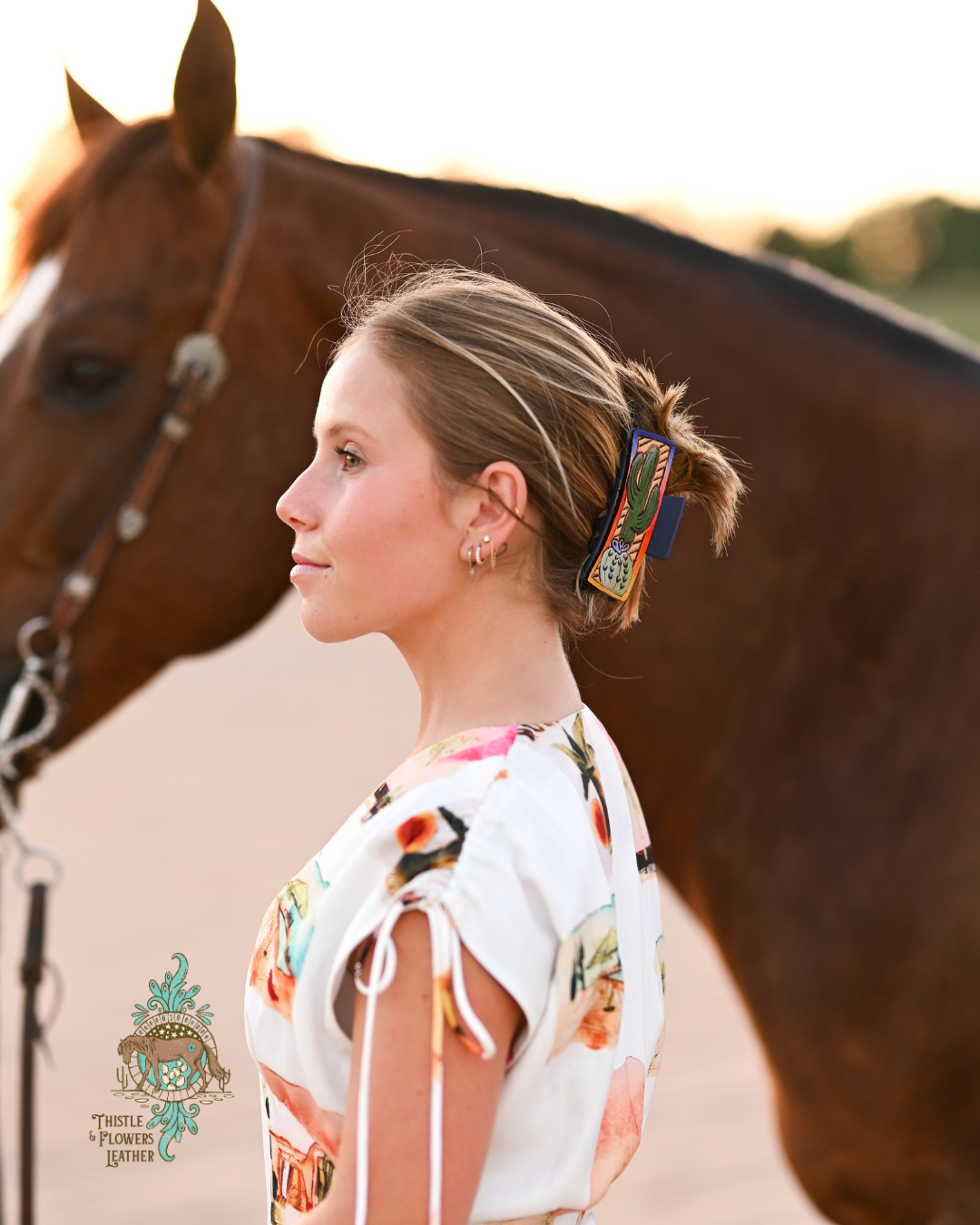 Blonde woman with horse, woman has a tooled and painted leather claw clip.  Clip has a sunset gradient on border of the clip, with 2 cacti on the inside.