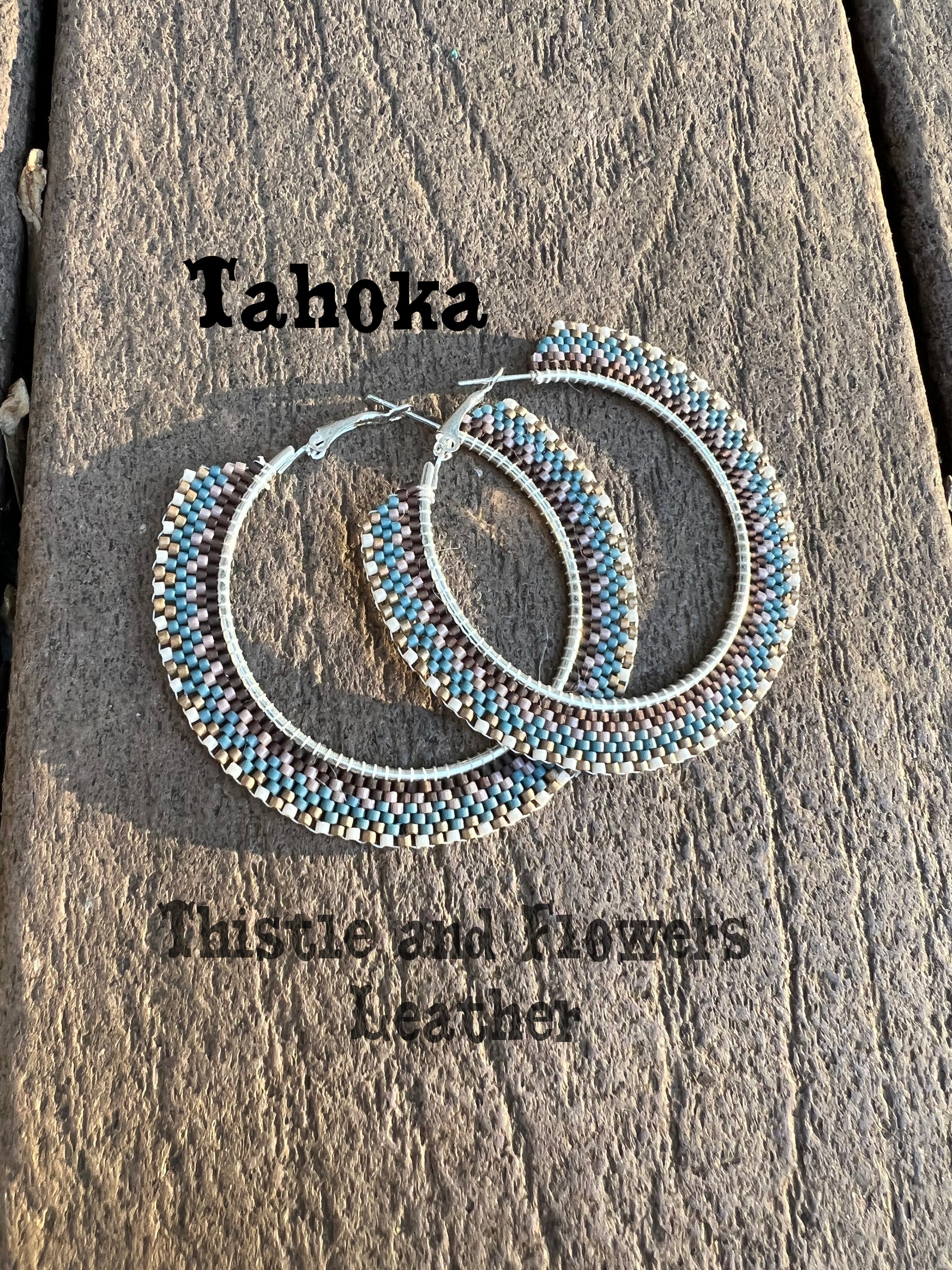 Beaded hoops. Silver colored hoop base. Intricate beaded pattern with chocolate, purple-grey, blue, matte metallic gold, and white beads. 